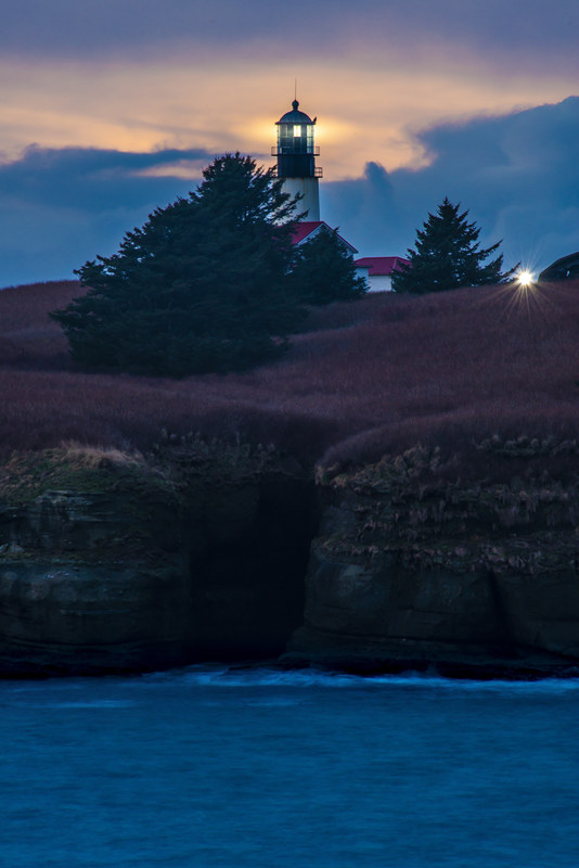 Cape Flattery lighthouse glowing at blue hour, perched on a dramatic coastal cliff